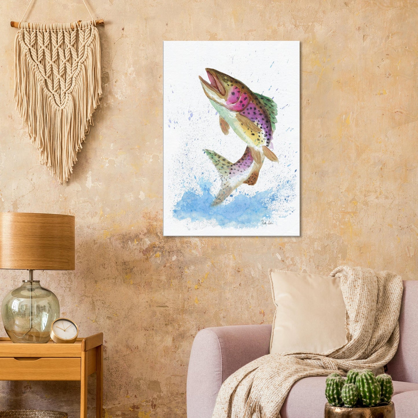 28 by 40 inch slim canvas wall art print featuring a watercolor painting of a rainbow trout leaping from the water. Shown on beige wall by macramé above pink sofa, wooden end table, and lamp.