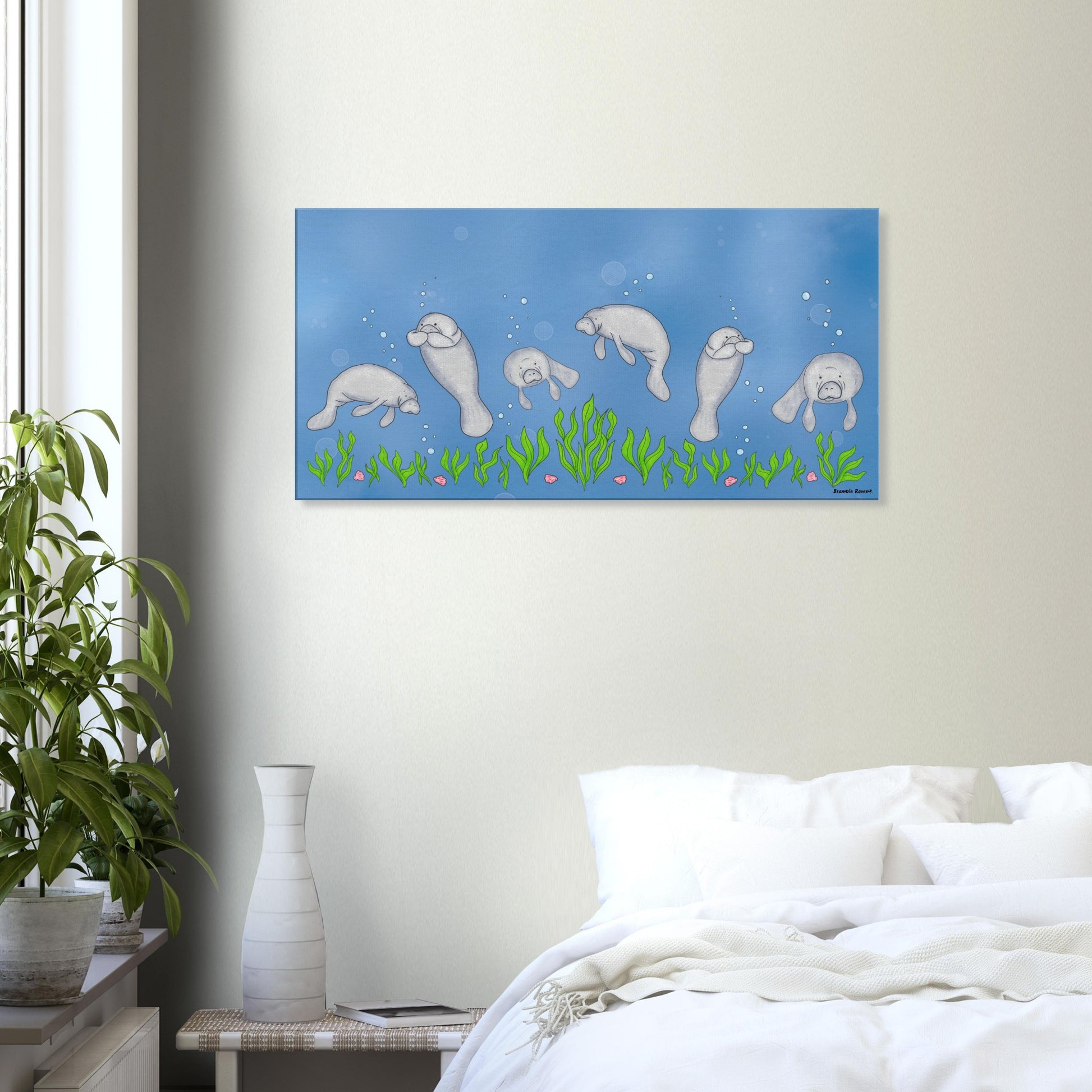 20 by 40 inch slim canvas wall art print featuring cute illustrated manatees swimming above the seabed.  Shown on wall above white bedding, side table, and potted plant.