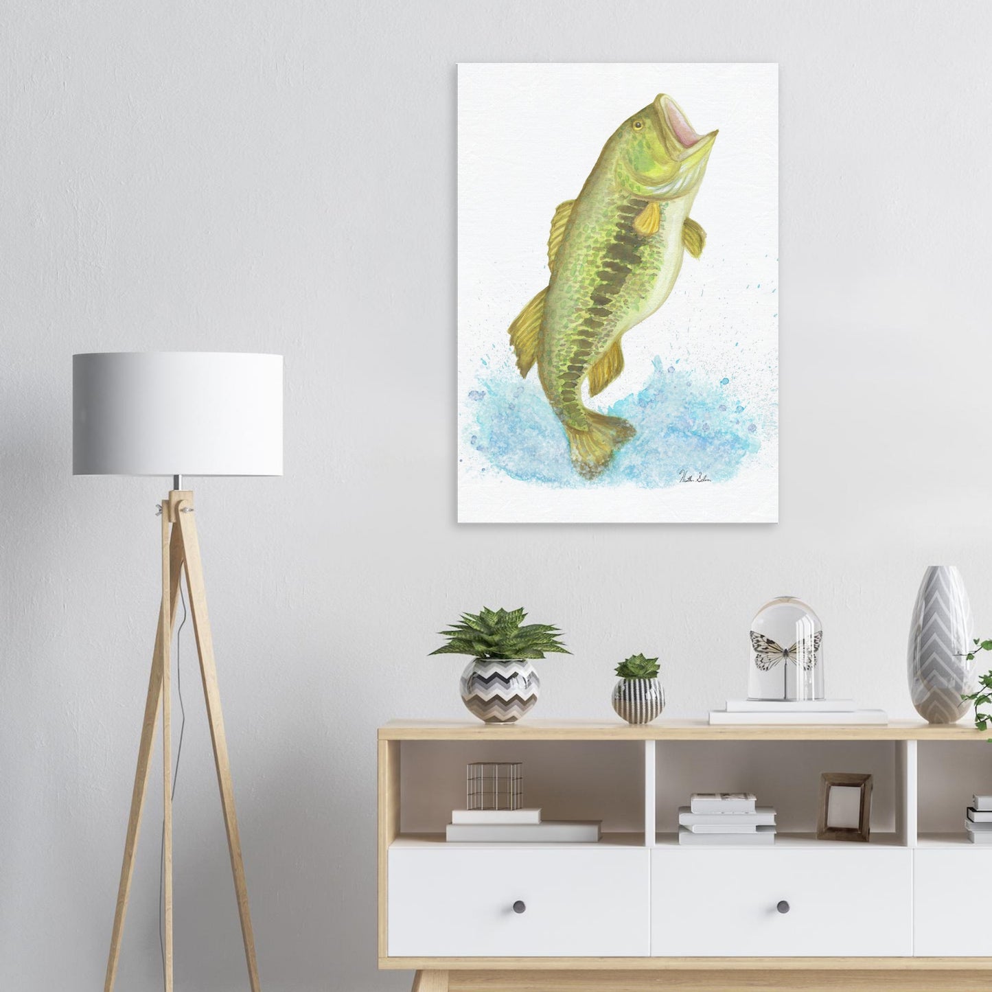 28 by 40 inch slim canvas wall art print featuring a watercolor painting of a largemouth bass leaping from the water. Shown on wall above wooden stand and lamp.