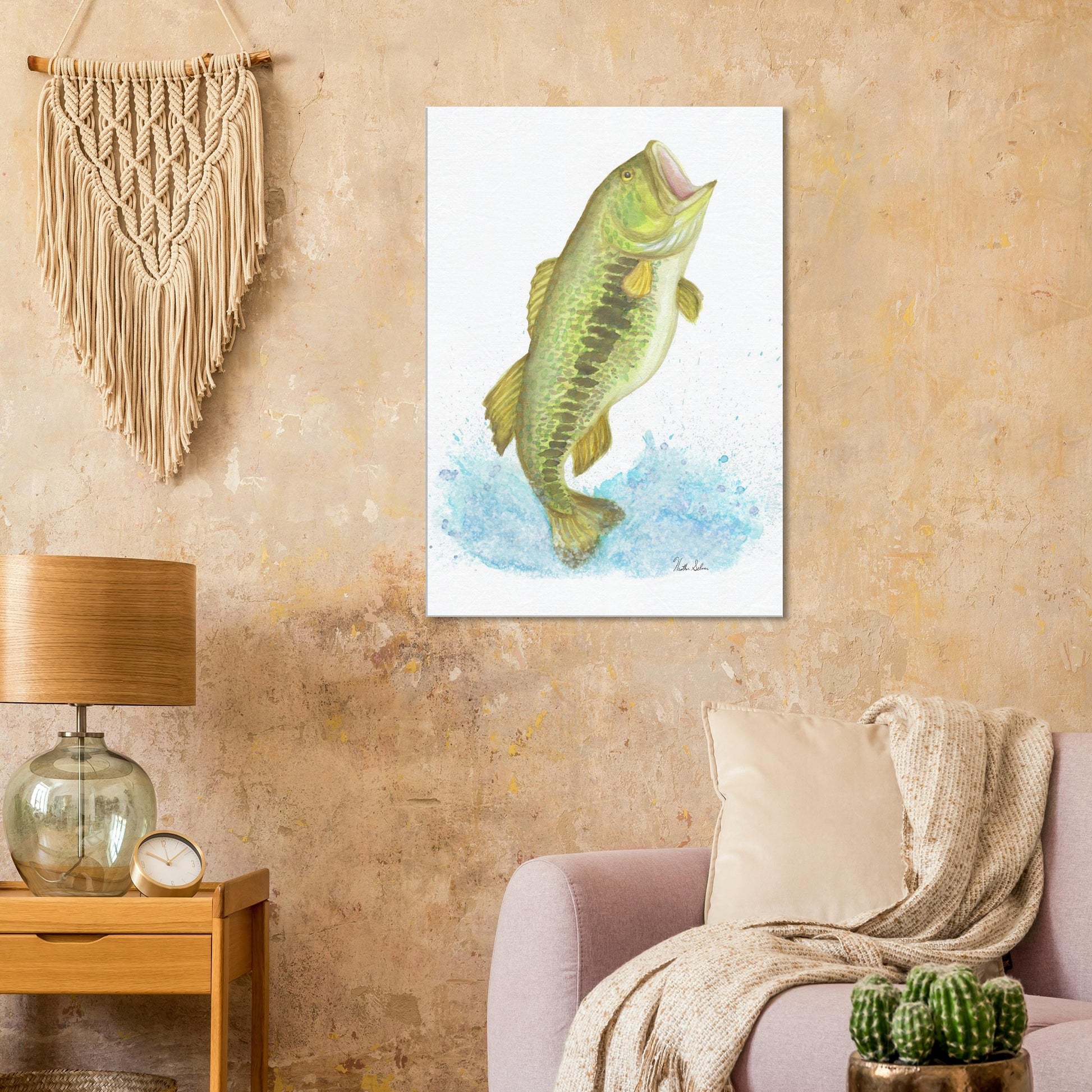 28 by 40 inch slim canvas wall art print featuring a watercolor painting of a largemouth bass leaping from the water. Shown on beige wall by macramé above pink sofa, side table and lamp.