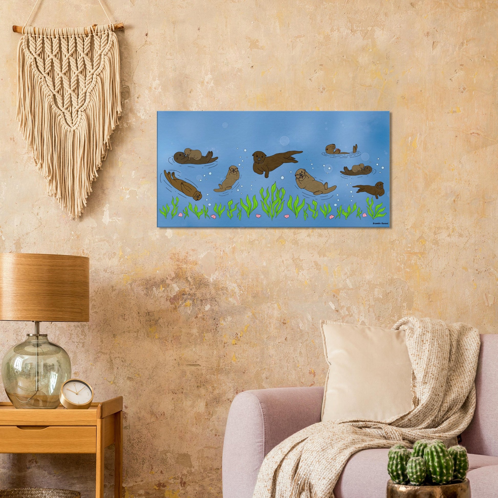 20 by 40 inch slim canvas wall art print of sea otters swimming along the seabed. Shown on beige wall by macramé, next to a wooden end table and lamp, and above a pink sofa.