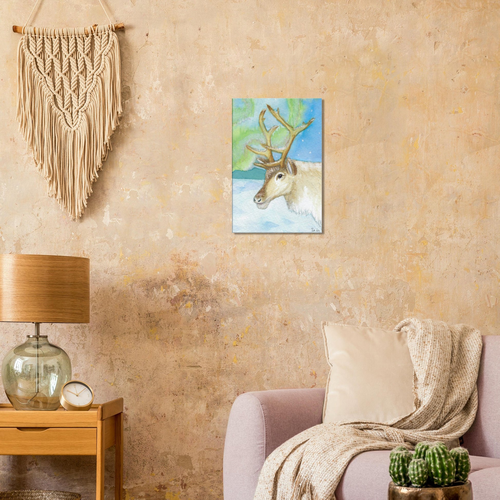 16 by 24 inch slim canvas print of Heather Silver's watercolor painting, northern lights reindeer. Shown on beige wall by macramé above pink sofa and wooden end table with lamp.