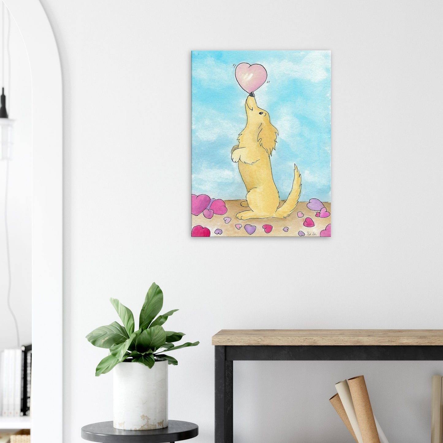 24 by 32 inch canvas wall art print of Heather Silver's watercolor painting, Puppy Love. It features a cute dog balancing a pink heart on its nose against a blue sky background. Canvas shown on wall above wooden end table and potted plant.