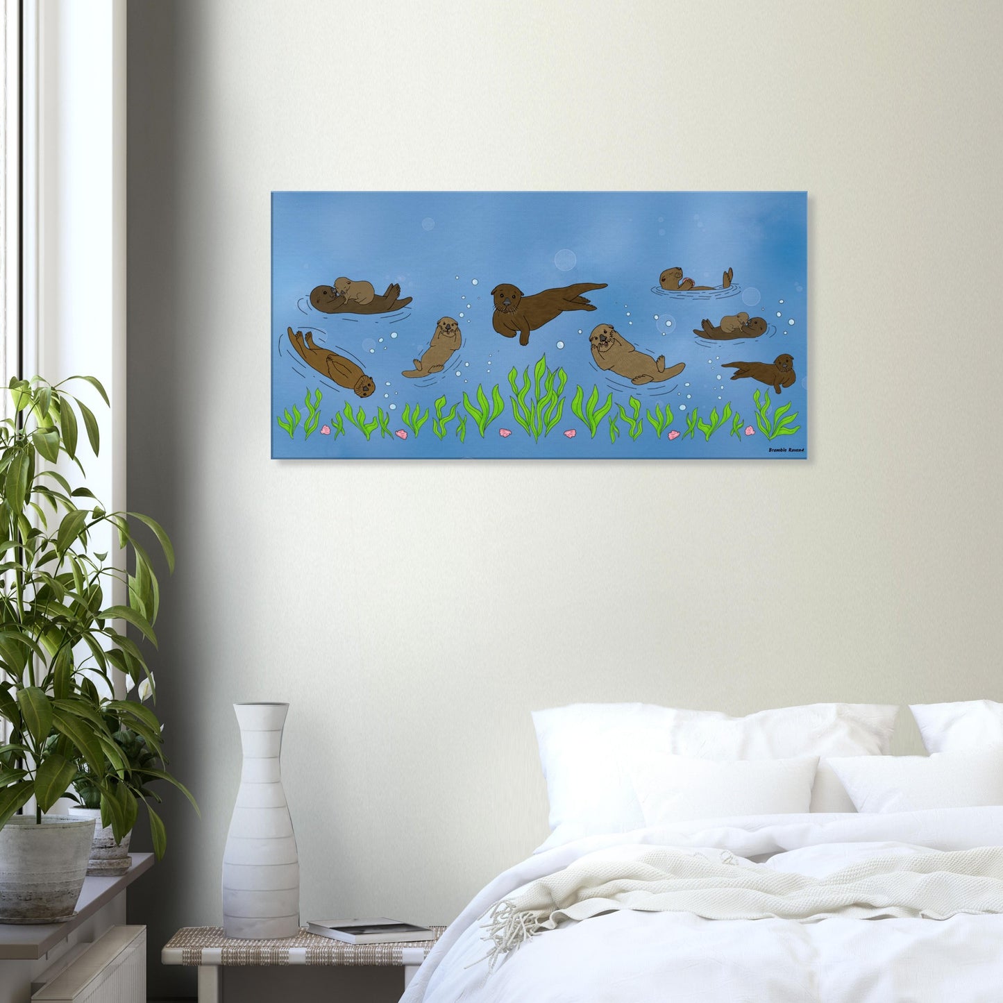 20 by 40 inch slim canvas wall art print of sea otters swimming along the seabed. Shown on wall above white bed, end table and potted plant.