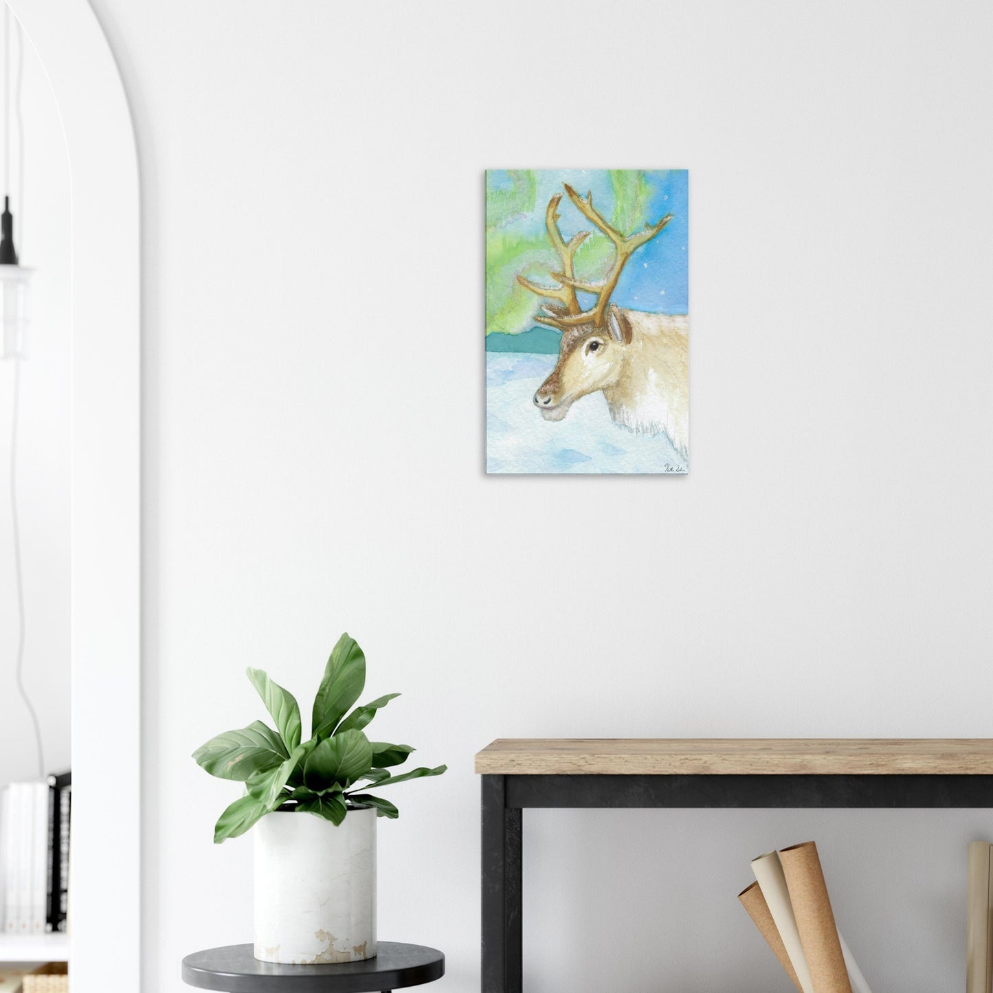 16 by 24 inch slim canvas print of Heather Silver's watercolor painting, northern lights reindeer. Shown on wall above wooden end table and potted plant.