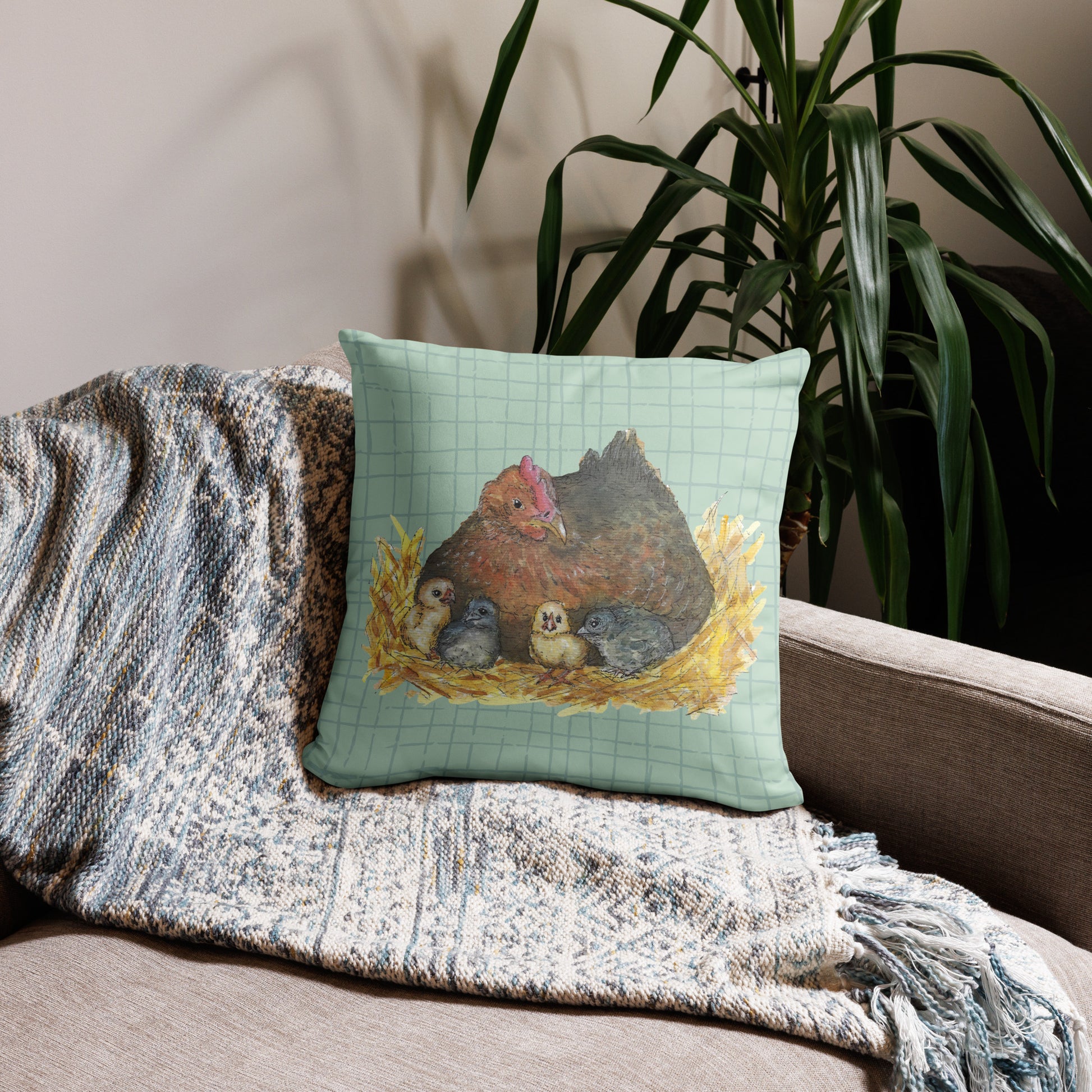 18 by 18 inch mother hen decorative throw pillow. Features Heather Silver's watercolor print of a mother hen and chicks on a green cross-hatched background. Image printed on both sides. Has a hidden zipper and washable cover. Comes with shape-retaining insert. Shown on throw blanket by potted plant.