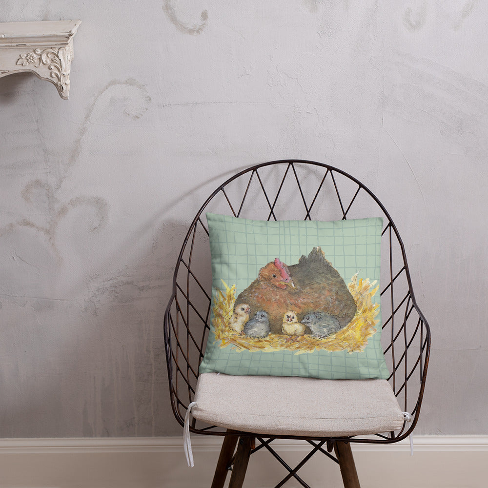 22 by 22 inch mother hen decorative throw pillow. Features Heather Silver's watercolor print of a mother hen and chicks on a green cross-hatched background. Image printed on both sides. Has a hidden zipper and washable cover. Comes with shape-retaining insert. Shown on wicker chair against wall.
