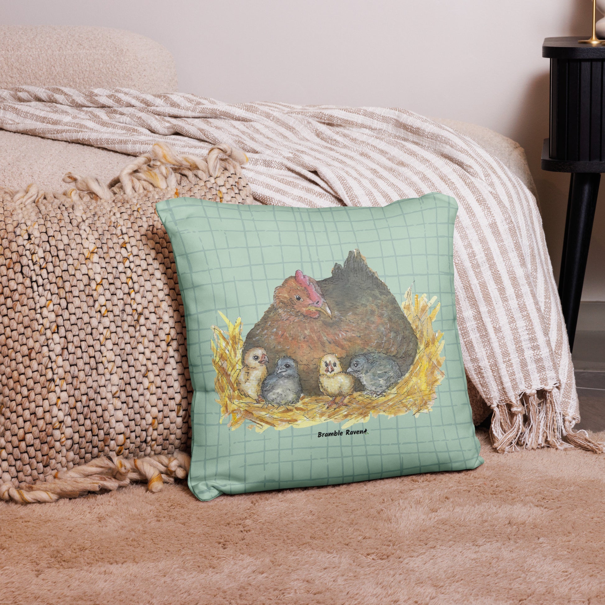 18 by 18 inch mother hen decorative throw pillow. Features Heather Silver's watercolor print of a mother hen and chicks on a green cross-hatched background. Image printed on both sides. Has a hidden zipper and washable cover. Comes with shape-retaining insert. Shown on tan carpet by beige bed.