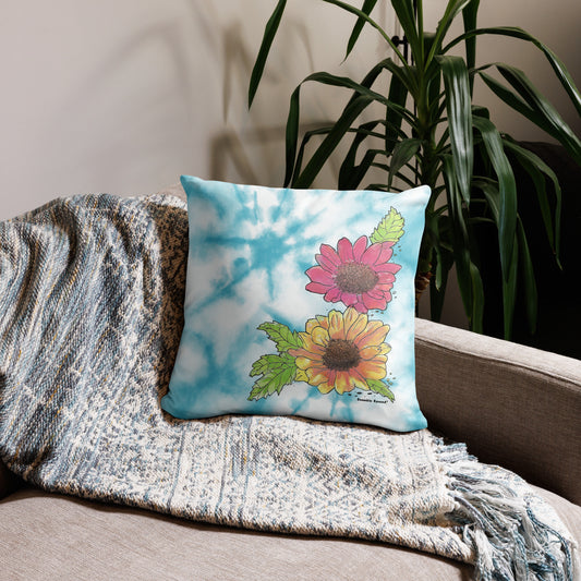 18 by 18 inch watercolor Gerber daisies throw pillow. Features large image of daisies against a watercolor blue background. Large image on front, small patterned image on back. Has hidden zipper and shape retaining insert. Shown on throw blanket on sofa.