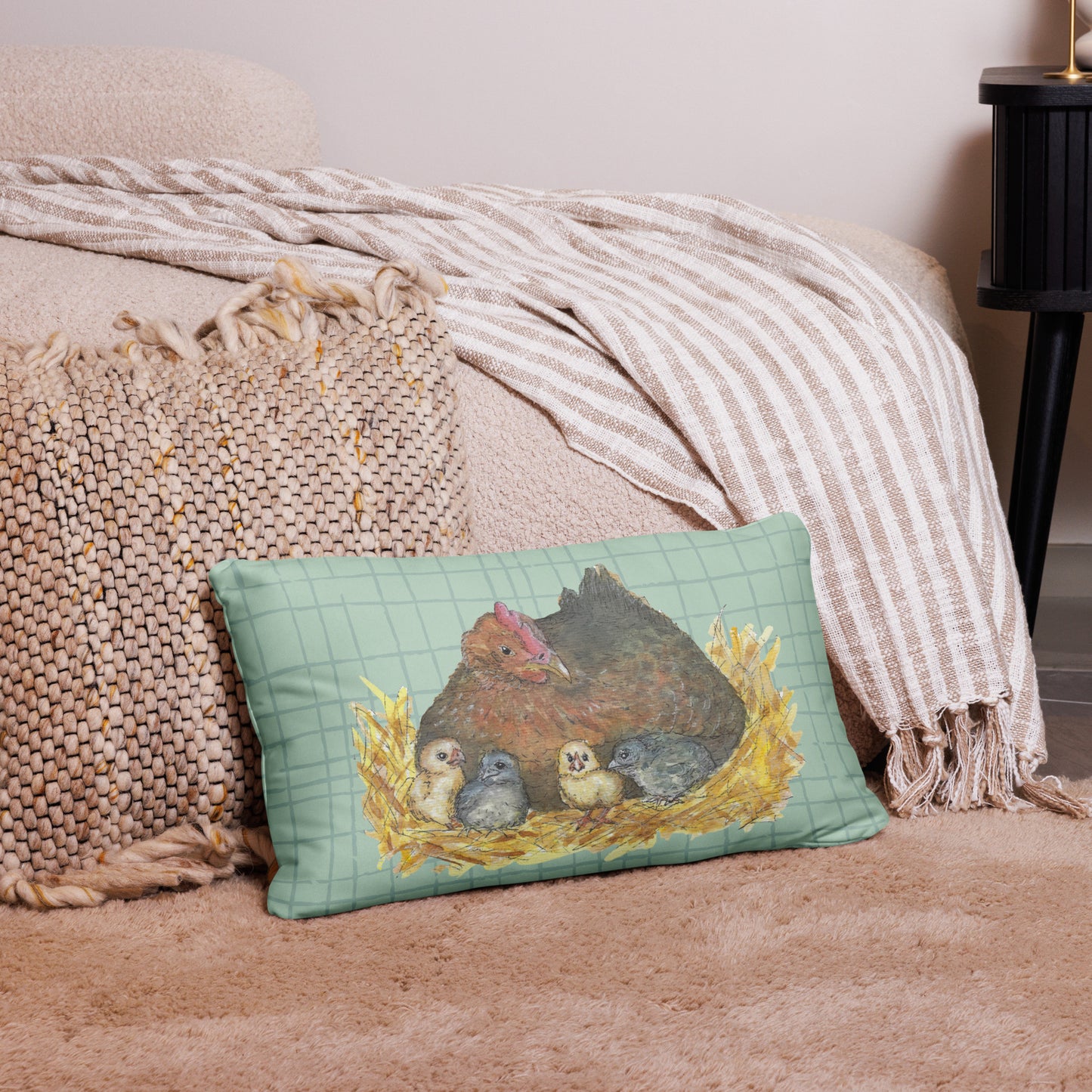 20 by 12 inch mother hen decorative throw pillow. Features Heather Silver's watercolor print of a mother hen and chicks on a green cross-hatched background. Image printed on both sides. Has a hidden zipper and washable cover. Comes with shape-retaining insert. Back view of pillow on tan carpet by beige bed.