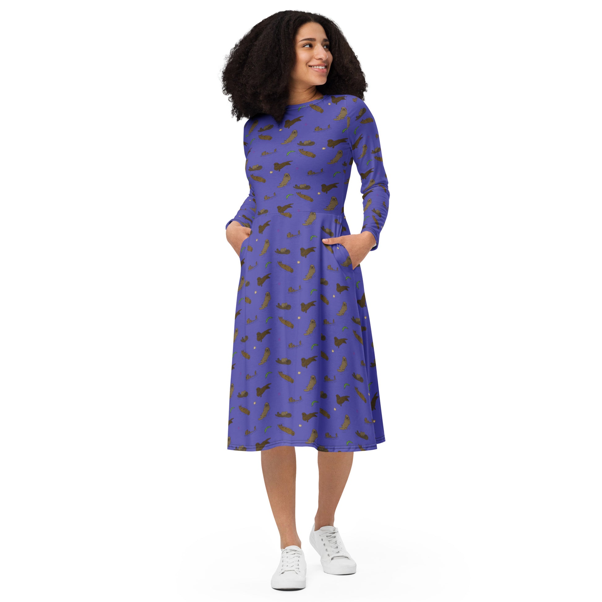 Long sleeve midi dress with fitted waist, flared bottom, and side pockets. Features a patterned design of sea otters, seashells, seaweed, and sea urchins on a purple background. Shown on female model.