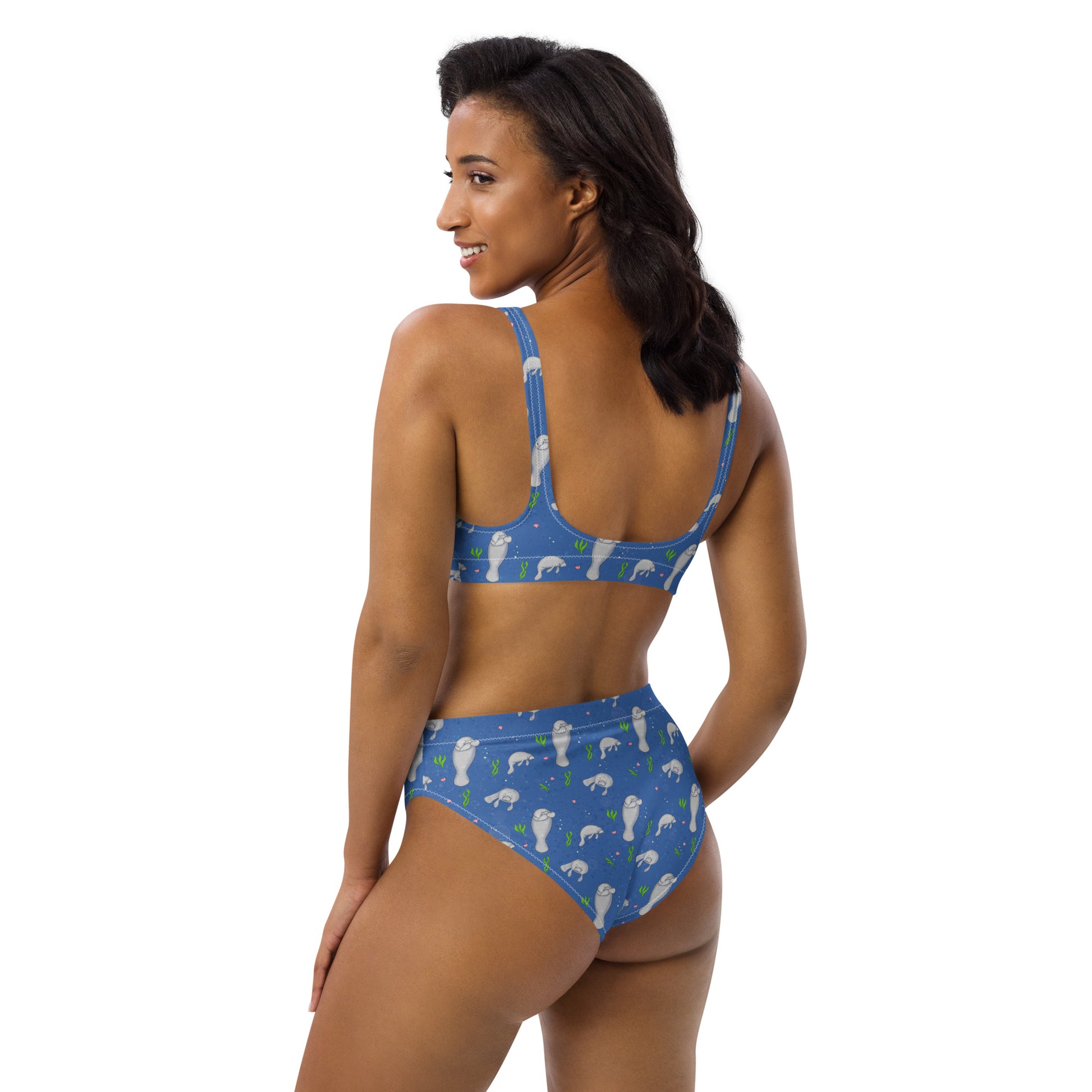 High-waisted bikini with hand-illustrated manatee pattern on a blue background. Made from recycled polyester combined with stretchable fabric. Has double layers and removable pads. Back view shown on female model facing left.