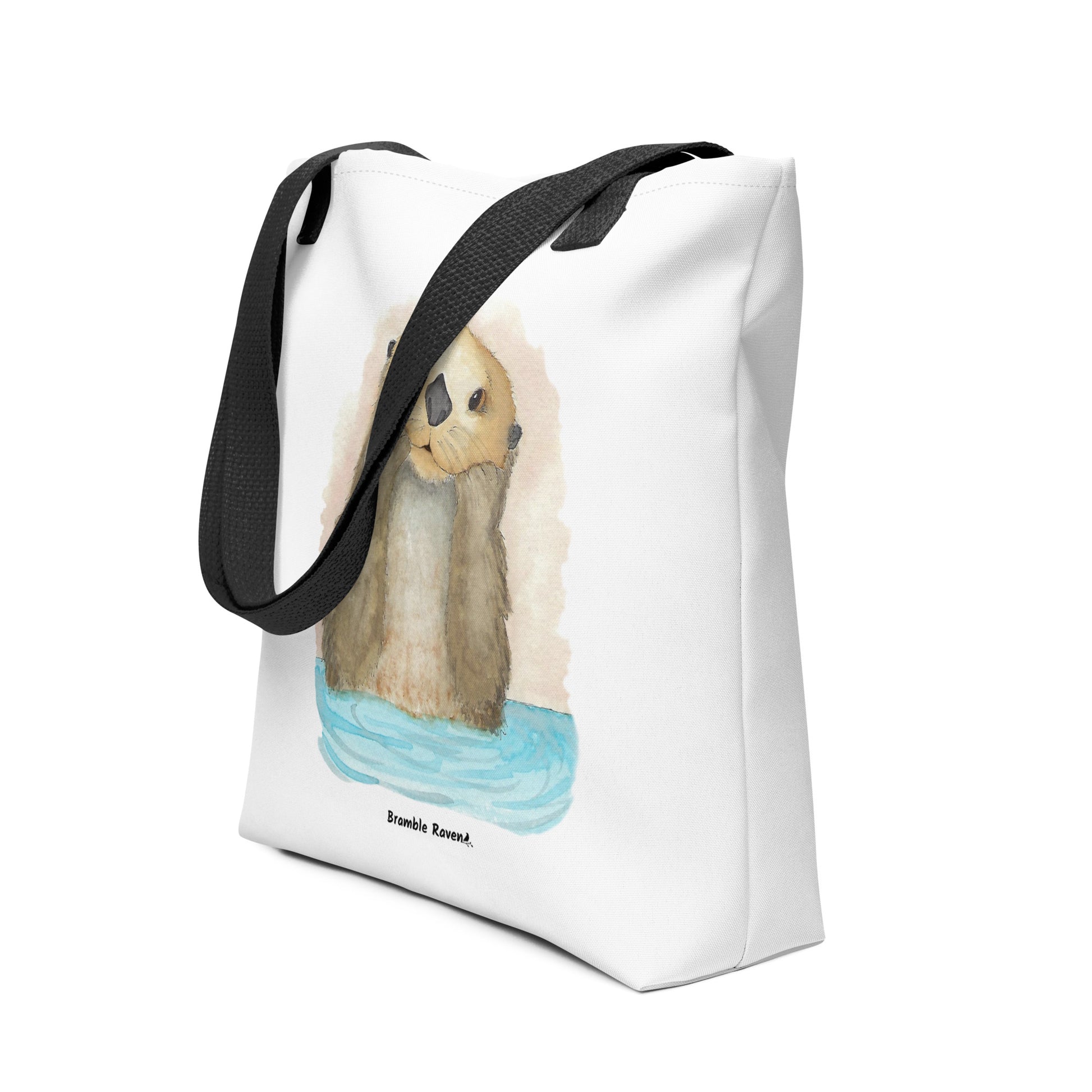 Otter Amazement sturdy tote bag. Measures 15" by 15" and can hold up to 44 lbs. Features watercolor sea otter painting printed on front and back. Has black handles. Shown sitting on the floor.
