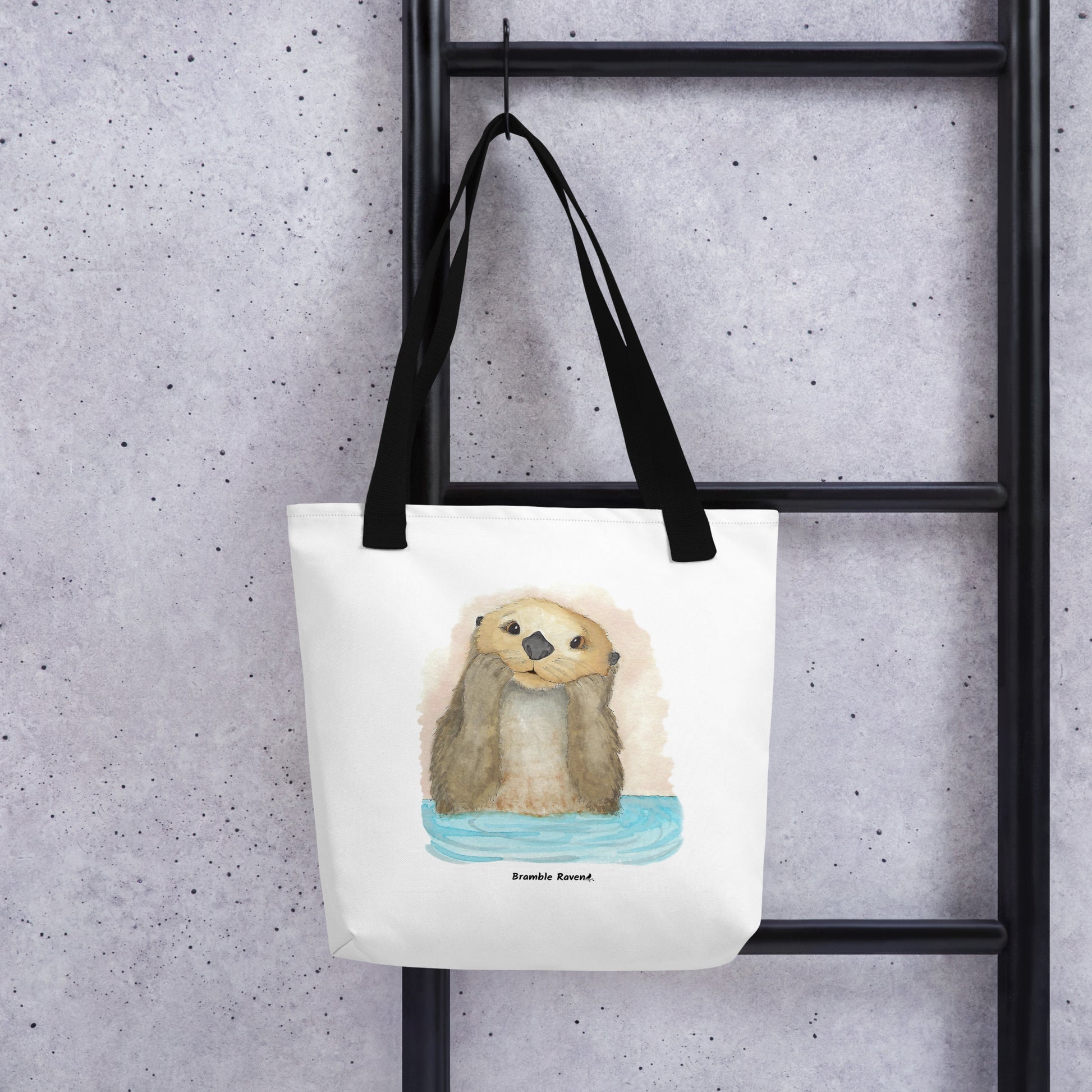 Otter Amazement sturdy tote bag. Measures 15" by 15" and can hold up to 44 lbs. Features watercolor sea otter painting printed on front and back. Has black handles. Shown hanging from a black ladder.
