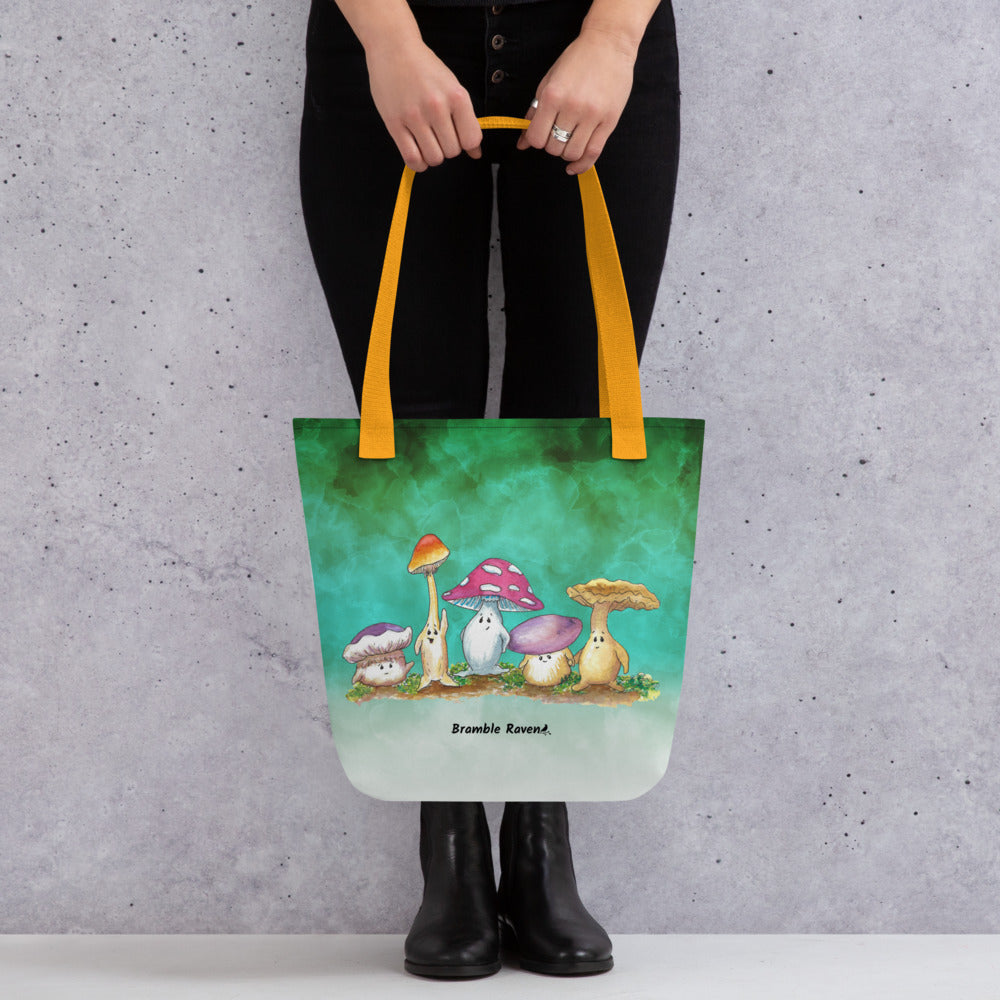 15 by 15 inch sturdy tote bag. Features Mushy and his whimsical mushroom friends on a green gradient background. Made of spun polyester with yellow cotton bull denim handles. Shown hanging from model's hands.