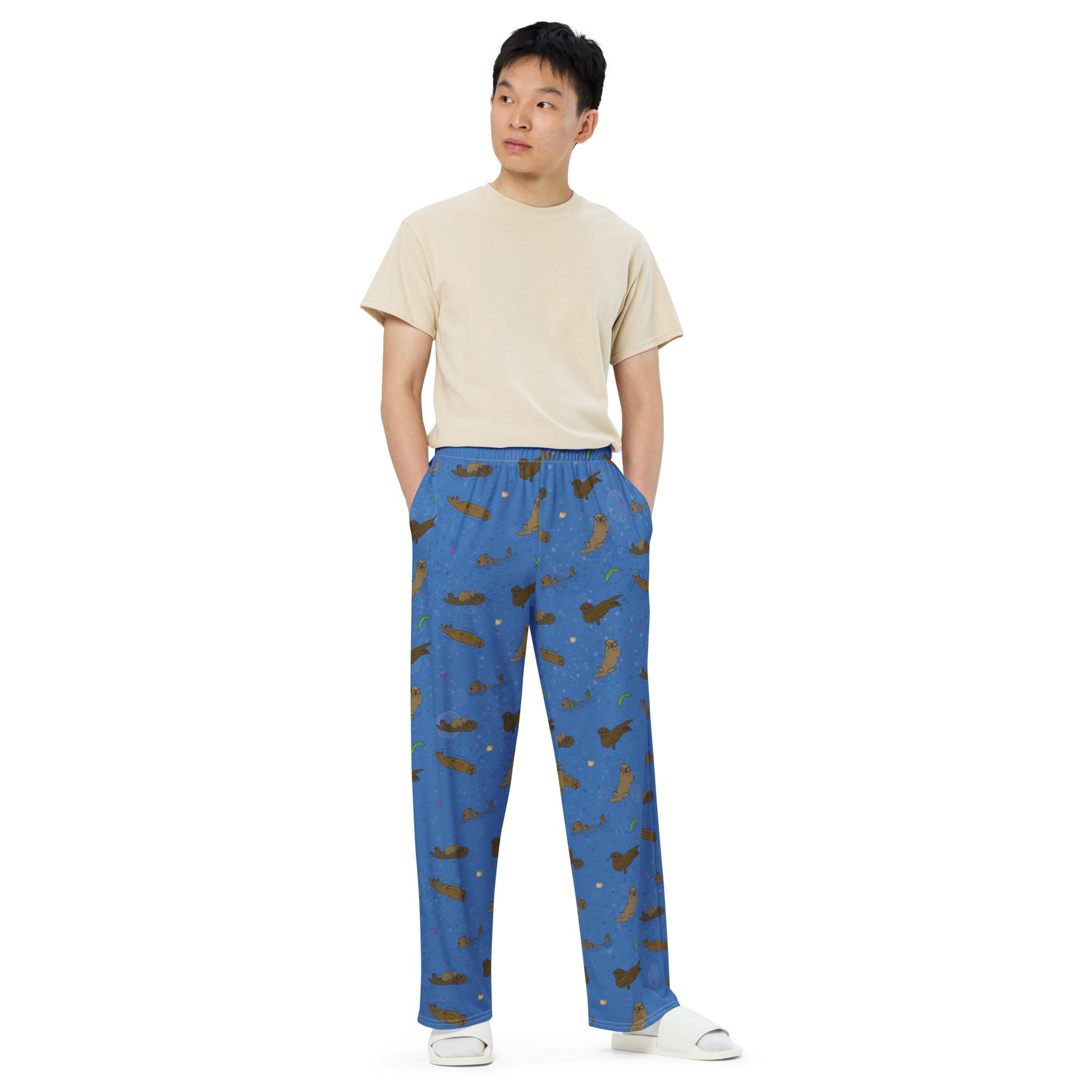 Unisex wide leg pants with elastic waistband, white drawstring and side pockets. Features a patterned design of sea otters, shells, seaweed and sea urchins on an ocean blue background. Shown on male model.