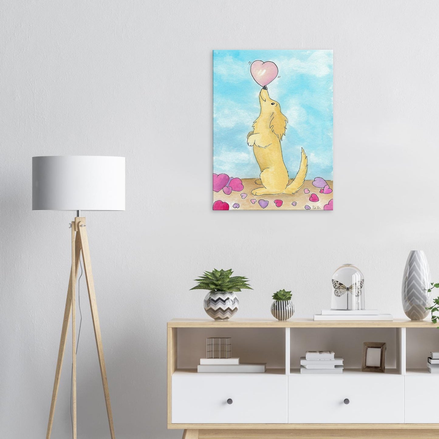 24 by 32 inch canvas wall art print of Heather Silver's watercolor painting, Puppy Love. It features a cute dog balancing a pink heart on its nose against a blue sky background. Canvas shown on wall above dresser with potted plants by a lamp.