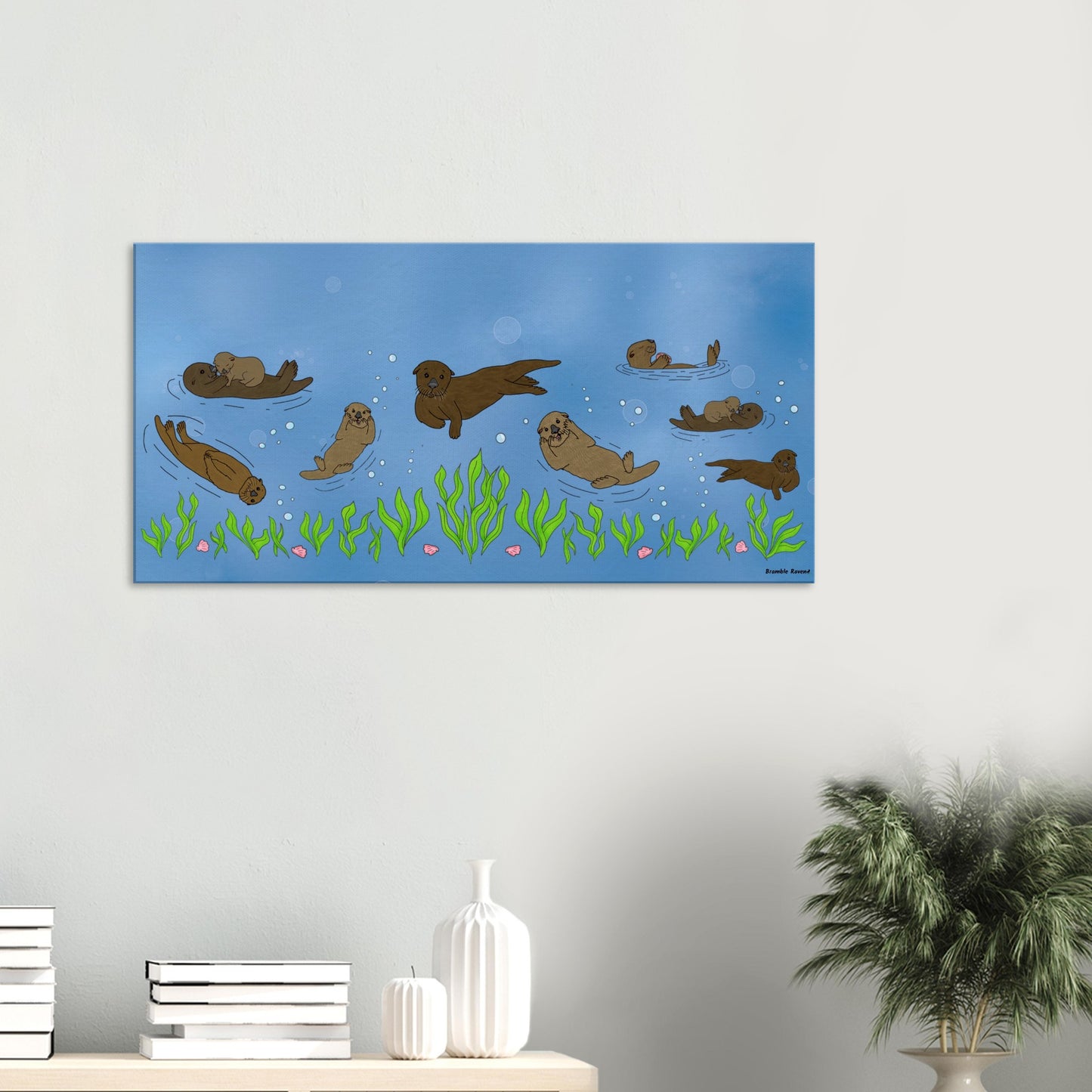 20 by 40 inch slim canvas wall art print of sea otters swimming along the seabed. Shown on wall above desktop with books and a potted plant.