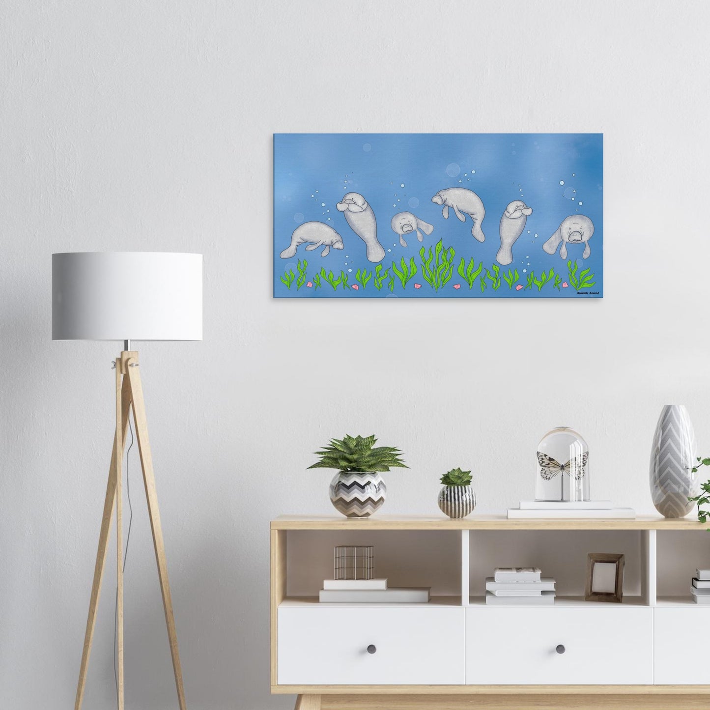 20 by 40 inch slim canvas wall art print featuring cute illustrated manatees swimming above the seabed. Shown on white wall above end table by a white lamp.
