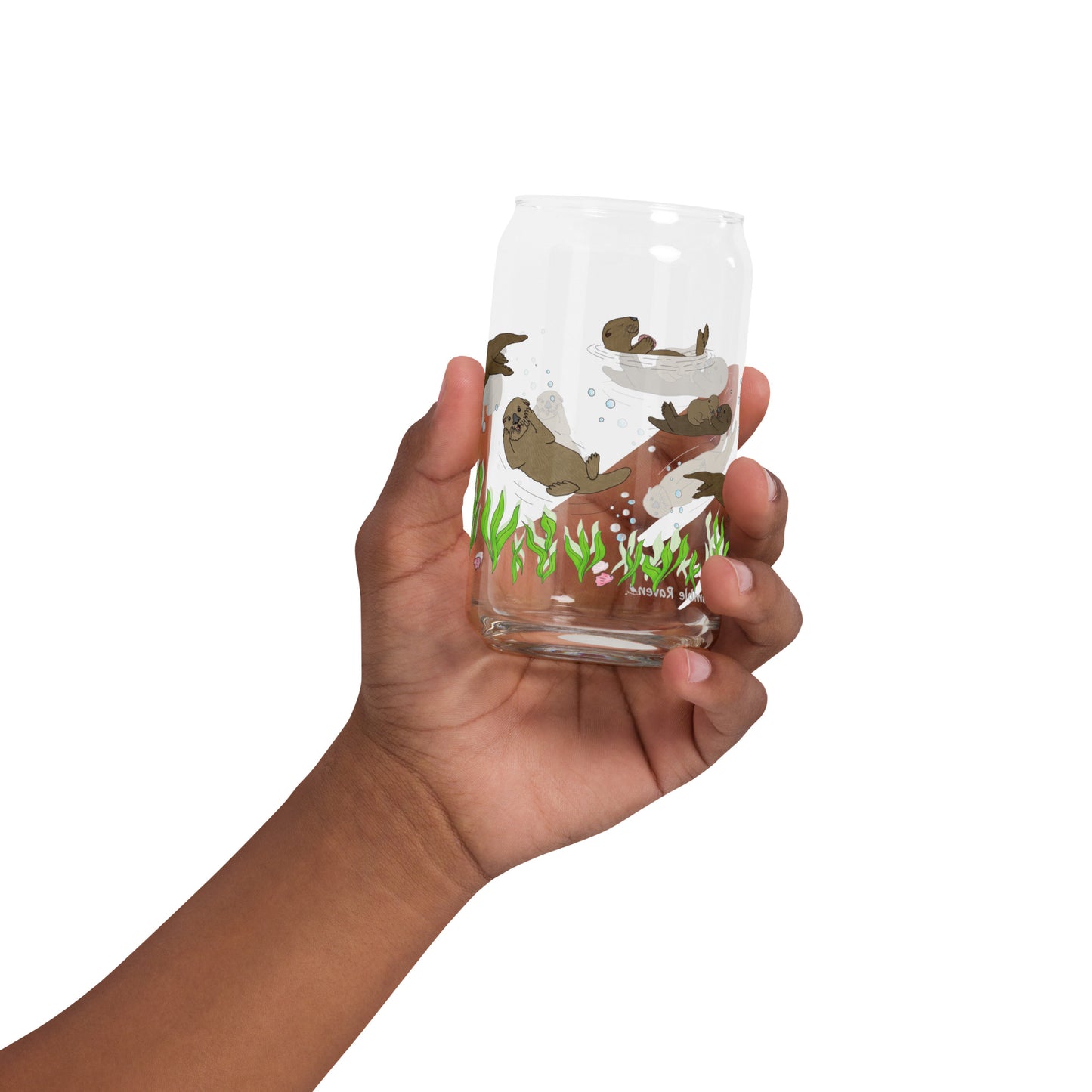 Can-shaped glass holds 16 fluid ounces. Has a design of sea otters swimming above the seaweed with bubble and shell accents. Shown in model's hand.