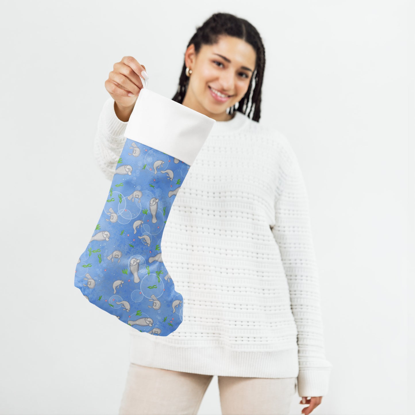 Limited Edition Manatee Christmas Stocking.  7 by 18 inches. The front has a hand-illustrated manatee design with an off-white polyester fabric on the back. It has a white fold-over cuff and a loop for hanging. Shown being held by female model.