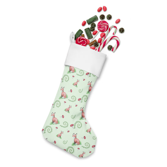 Limited Edition Forest Fox Christmas Stocking.  7 by 18 inches. The front has a patterned watercolor fox design with mushrooms and ferns on a green background and an off-white polyester back fabric. It has a white fold-over cuff and a hanging loop. Shown stuffed with candy.