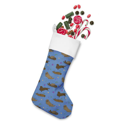 Limited Edition Sea Otter Christmas Stocking.  7 by 18 inches. The front has a hand-illustrated sea otter design with an off-white polyester fabric on the back. It has a white fold-over cuff and a loop for hanging. Shown stuffed with candy.