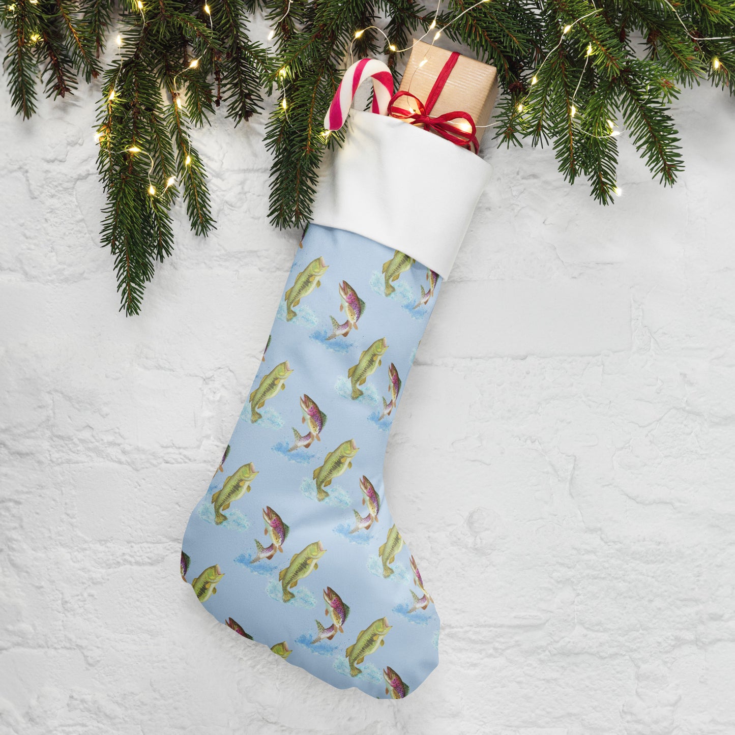 Limited Edition Blue Fishing Christmas Stocking.  7 by 18 inches. The front has watercolor rainbow trout and largemouth bass patterned on a blue background and an off-white polyester back fabric. It has a white fold-over cuff and a hanging loop. Shown stuffed with gifts by pine boughs.