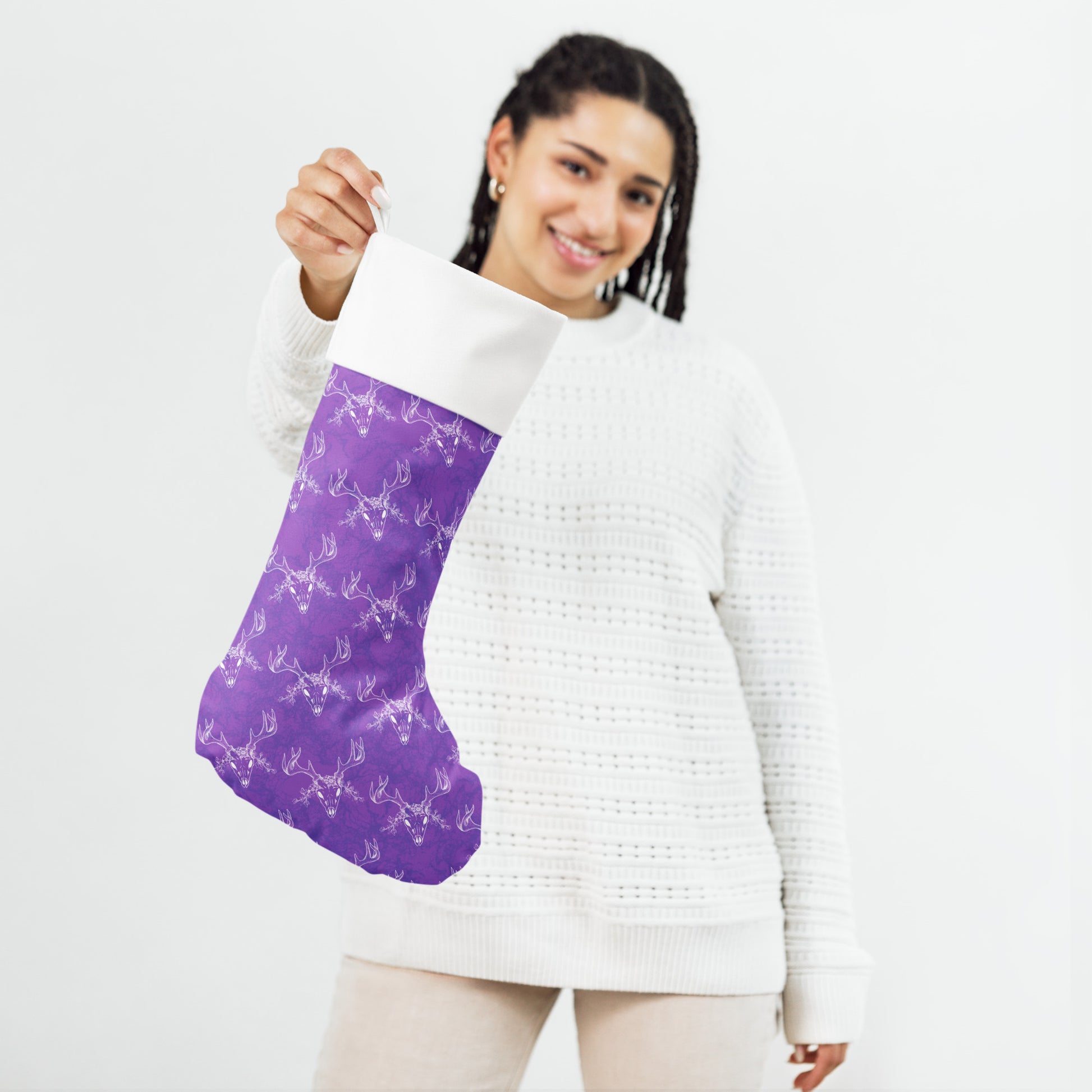 Limited Edition Purple Deer Skull Christmas Stocking.  7 by 18 inches. The front has a hand-illustrated deer skull design on a purple background with an off-white polyester fabric on the back. It has a white fold-over cuff and a loop for hanging. Shown being held by female model.