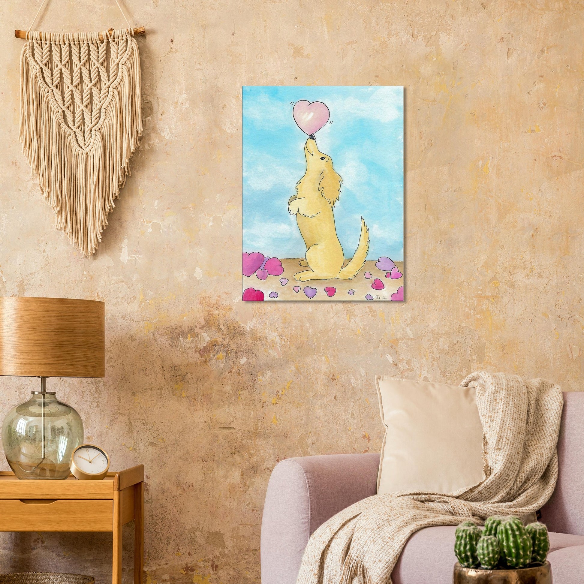 24 by 32 inch canvas wall art print of Heather Silver's watercolor painting, Puppy Love. It features a cute dog balancing a pink heart on its nose against a blue sky background. Canvas shown on beige wall by macramé above pink sofa and wooden end table with lamp.