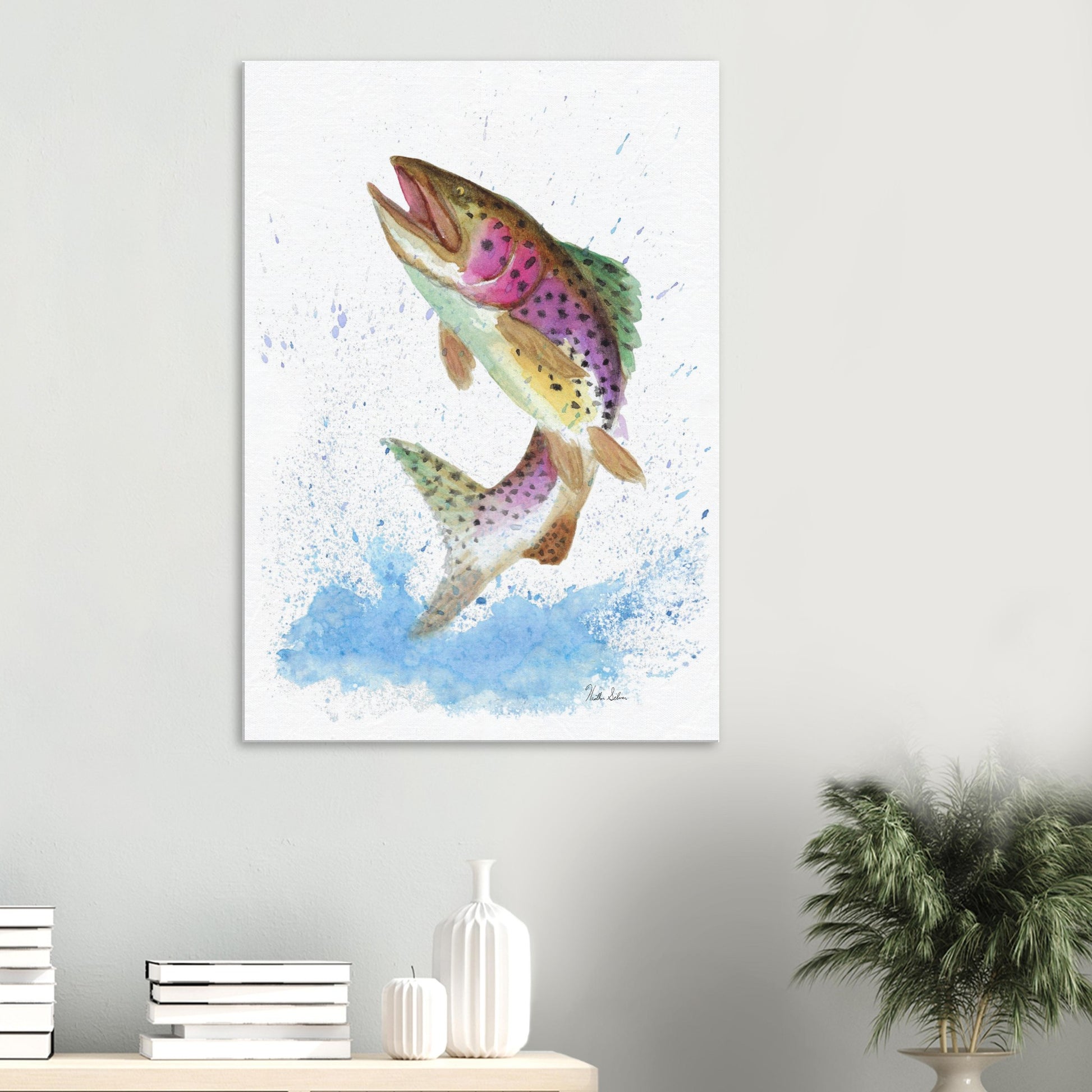 28 by 40 inch slim canvas wall art print featuring a watercolor painting of a rainbow trout leaping from the water. Shown on wall above tabletop with books and potted plant.