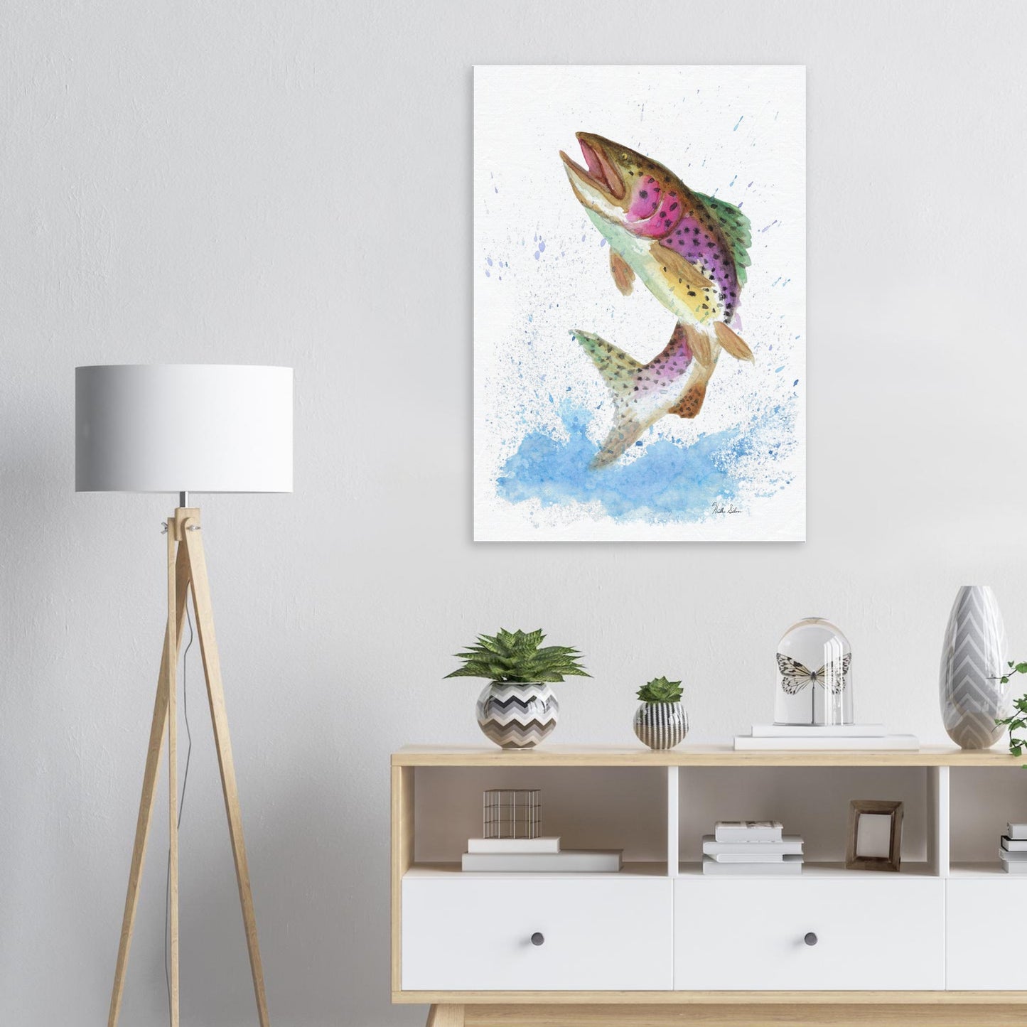 28 by 40 inch slim canvas wall art print featuring a watercolor painting of a rainbow trout leaping from the water. Shown on wall above wooden shelves, lamp, and potted plants.