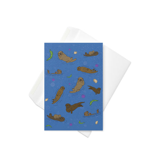 Sea Otter Jamboree greeting card. 4x6 inches tall. Shows hand illustrated front of sea otters with seaweed, shells, and sea urchins on an ocean blue background. Inside is blank. Comes with complimentary envelope.