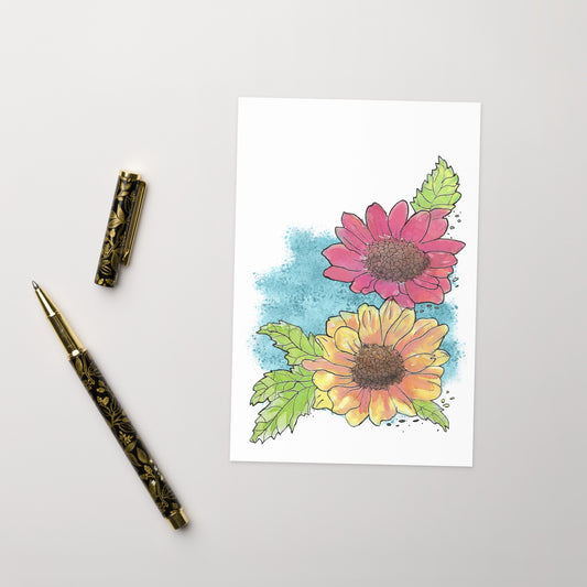 4 by 6 inch watercolor Gerber daisies greeting card and envelope. Has watercolor daisies on the front. The inside has a blue watercolor border with daisy accents and room for a message. Image shows card front by ballpoint pen.