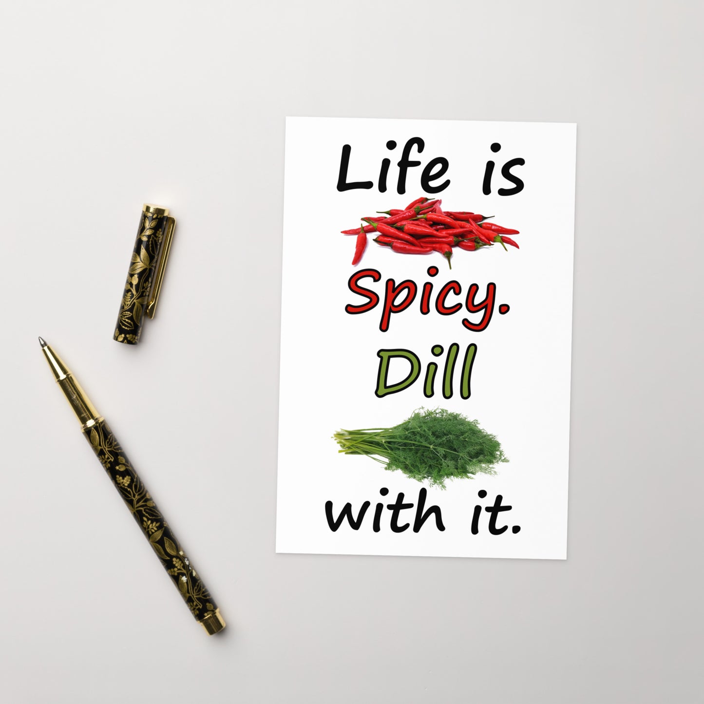 4 by 6 inch Life Is Spicy greeting card. Features Life is Spicy, Dill With It text, with image of chili peppers and dill weed on the front. The inside is blank. Comes with a white envelope. Card is made of durable paperboard with vibrant printing. Shown on tabletop next to ballpoint pen.
