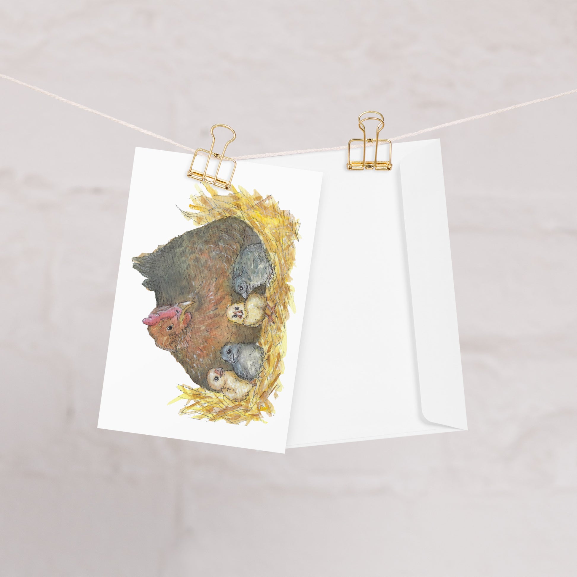 4 by 6 inch greeting card and envelope. Front features watercolor print of a mother hen and four chicks in a nest. Inside is blank. Image shows card and enveloped clipped to a string.