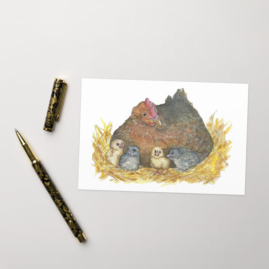 4 by 6 inch greeting card. Comes in set of ten cards and ten envelopes. Front features watercolor print of a mother hen and her four chicks in a straw nest. Inside is blank. Photo shows greeting card on tabletop by a ballpoint pen.
