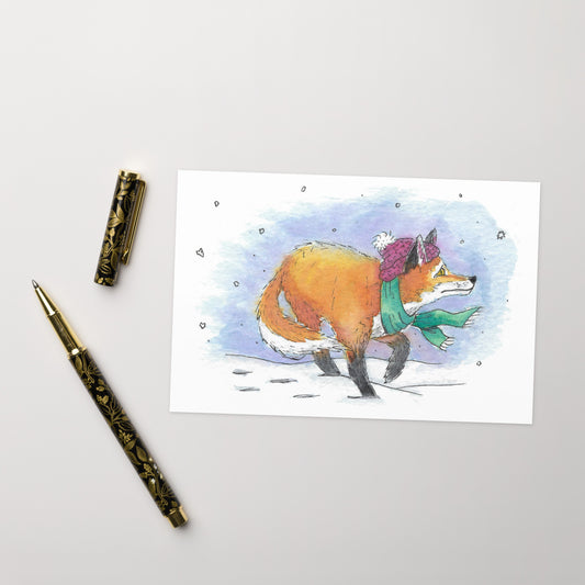 4.25 by 5.5 inch greeting card set. Comes with 10 greeting cards and envelopes. Front features watercolor illustration of a winter fox with his hat and scarf in the snow. Made of uncoated 300gsm 110 lb paperboard with vibrant printing. Inside is blank for your message. Shown on tabletop by ballpoint pen.