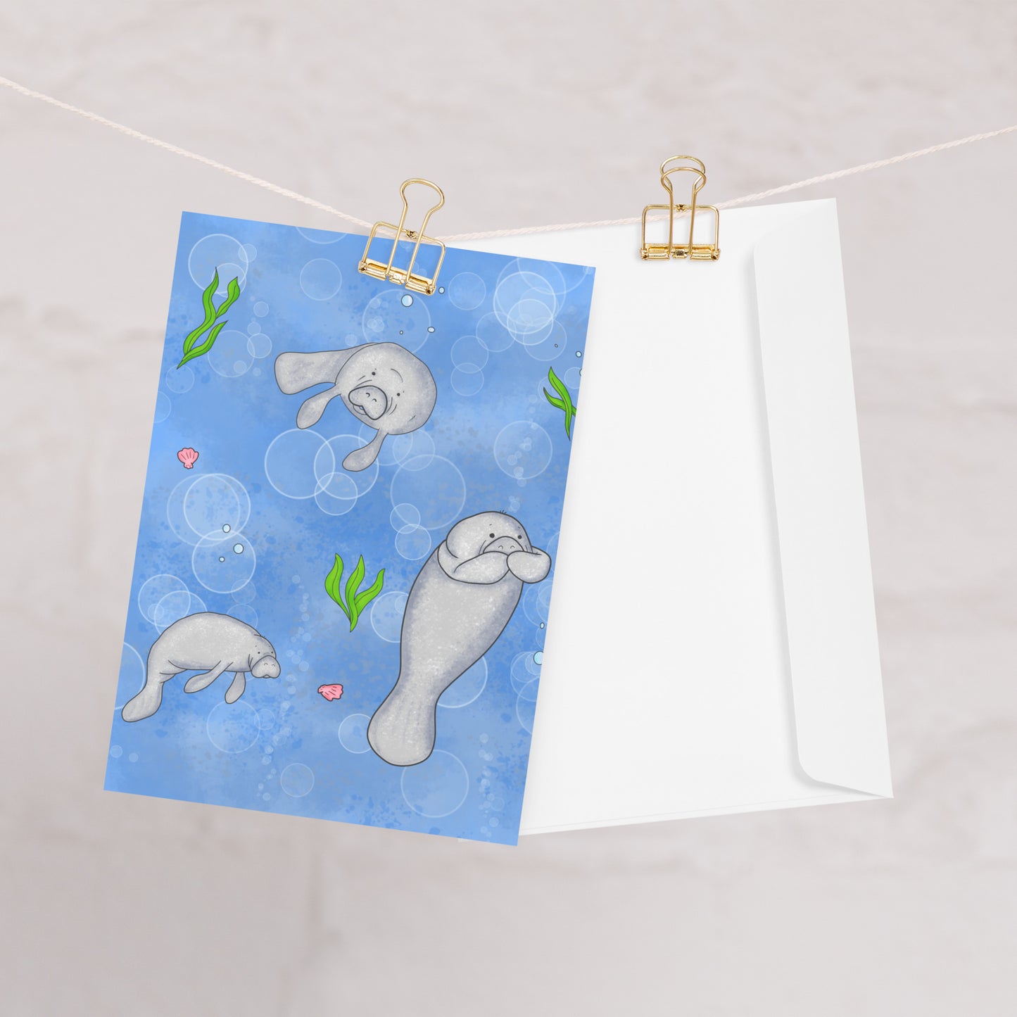 Pack of ten 5 x 7 inch greeting cards. Features illustrated roly-poly manatees on the front. Inside is blank. Made of coated paperboard. Comes with ten envelopes. One card shown on clothesline with white envelope.