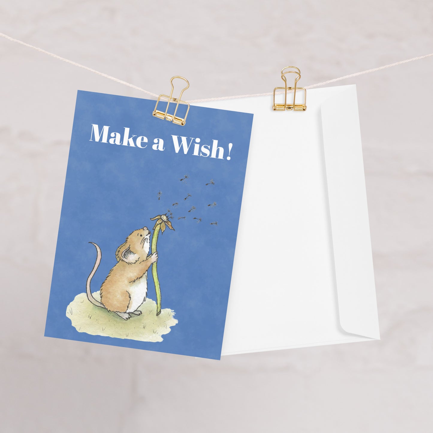 Ten fun greeting cards with ten envelopes. The front features white "Make a wish!" text and our watercolor dandelion wish mouse on a blue background. Inside is blank. Made with thick 350 gsm 150lb coated paperboard with vibrant printing.  Cards measure 5 by 7 inches. One card shown on clothesline with white envelope.