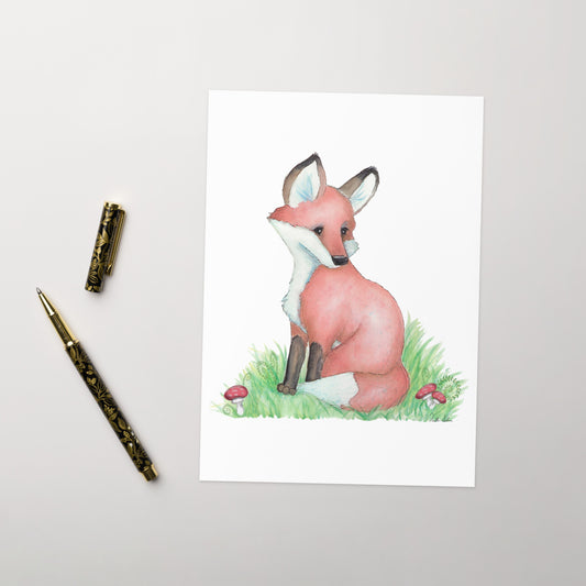 Pack of ten 5 x 7 inch greeting cards with envelopes. Front of card has watercolor fox nestled in the grass by mushrooms and ferns. Inside is blank. Cards are 130 lb 350 gsm coated paperboard with vibrant printing.  Shown on tabletop by ballpoint pen.