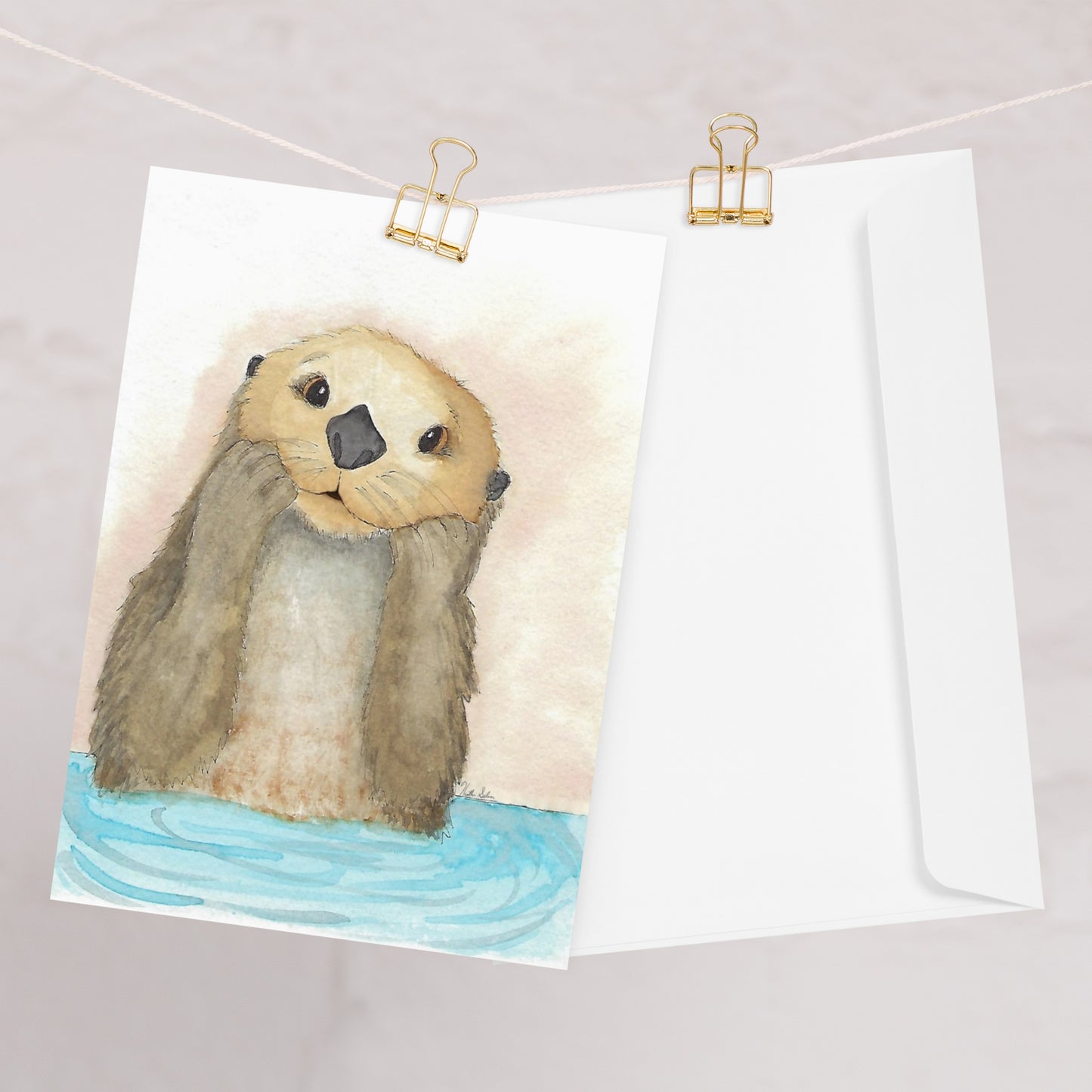 Pack of ten 5 x 7 inch greeting cards. Features watercolor print of a playful sea otter on the front. Inside is blank. Made of coated paperboard. Comes with ten envelopes. One card shown on clothesline with a white envelope.
