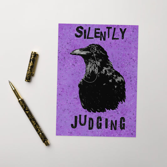 Ten humorous greeting cards with ten envelopes. The front features our silently judging crow with a monocle on a purple textured background. Inside is blank. Made with thick 350 gsm 150lb coated paperboard with vibrant printing.  The cards measure 5 by 7 inches. Shown on tabletop by ballpoint pen.
