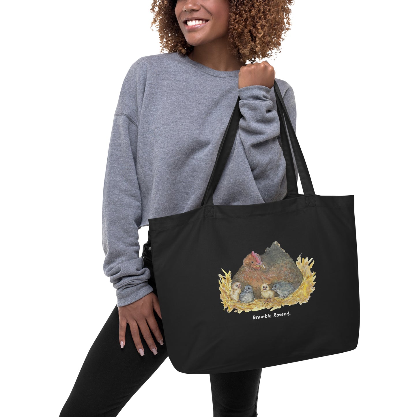 Large black organic cotton tote bag. Has a watercolor mother hand and chicks print. Holds up to 30 pounds. Shown being held by female model.