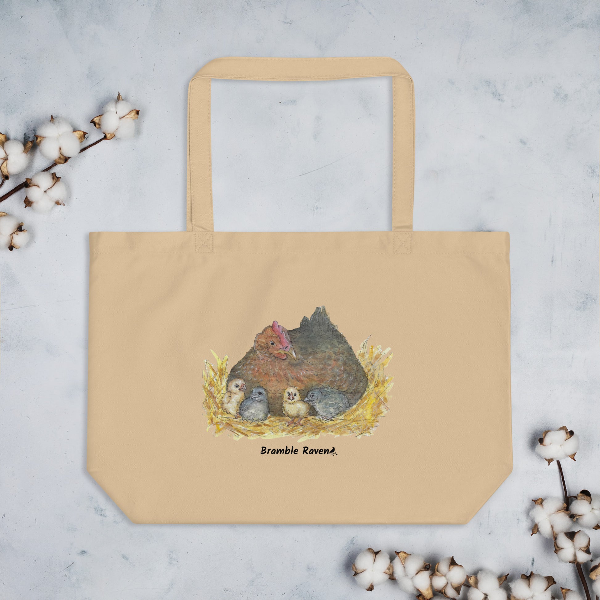 Large tan organic cotton tote bag. Has a watercolor mother hand and chicks print. Holds up to 30 pounds. Shown on tabletop by cotton plants.