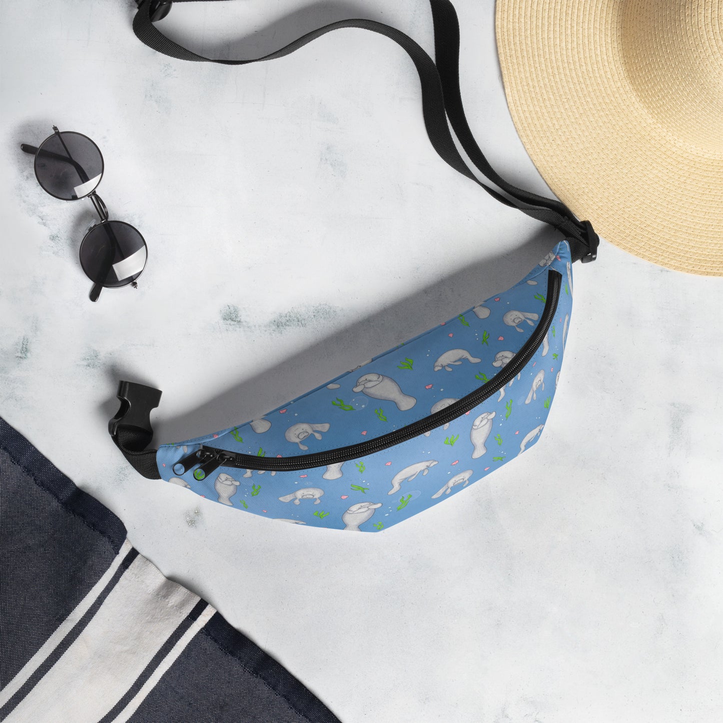 Cute manatee patterned belt bag with adjustable straps, zippered pouch, and small inner pocket. Shown next to sunhat and sunglasses.