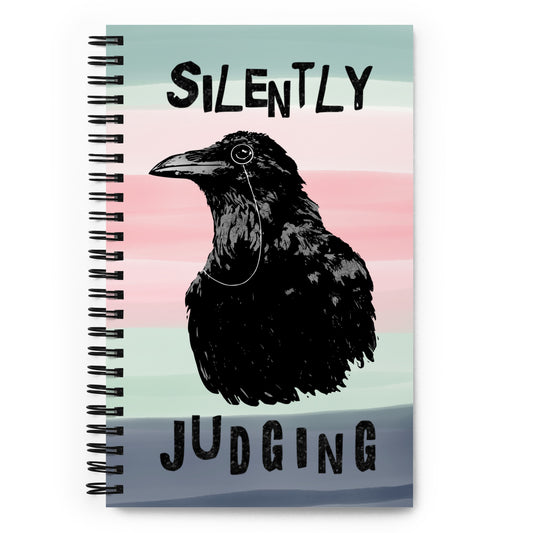 Spiral bound notebook with soft touch cover and 140 dotted pages. Cover features silently judging text and monocled crow on a striped background. Measures 5.5 inches by 8.5 inches.