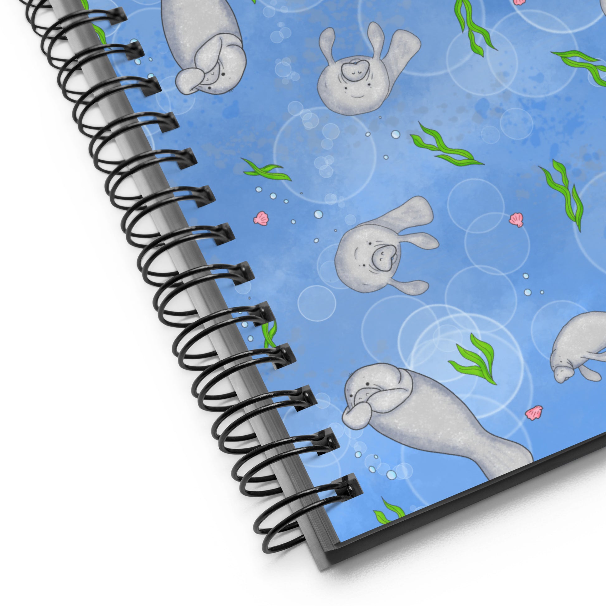 Spiral bound notebook with soft touch cover and 140 dotted pages. Cover features cute illustrated manatees swimming in the water. Measures 5.5 inches by 8.5 inches. Detail view of metal spiral binding and cover.