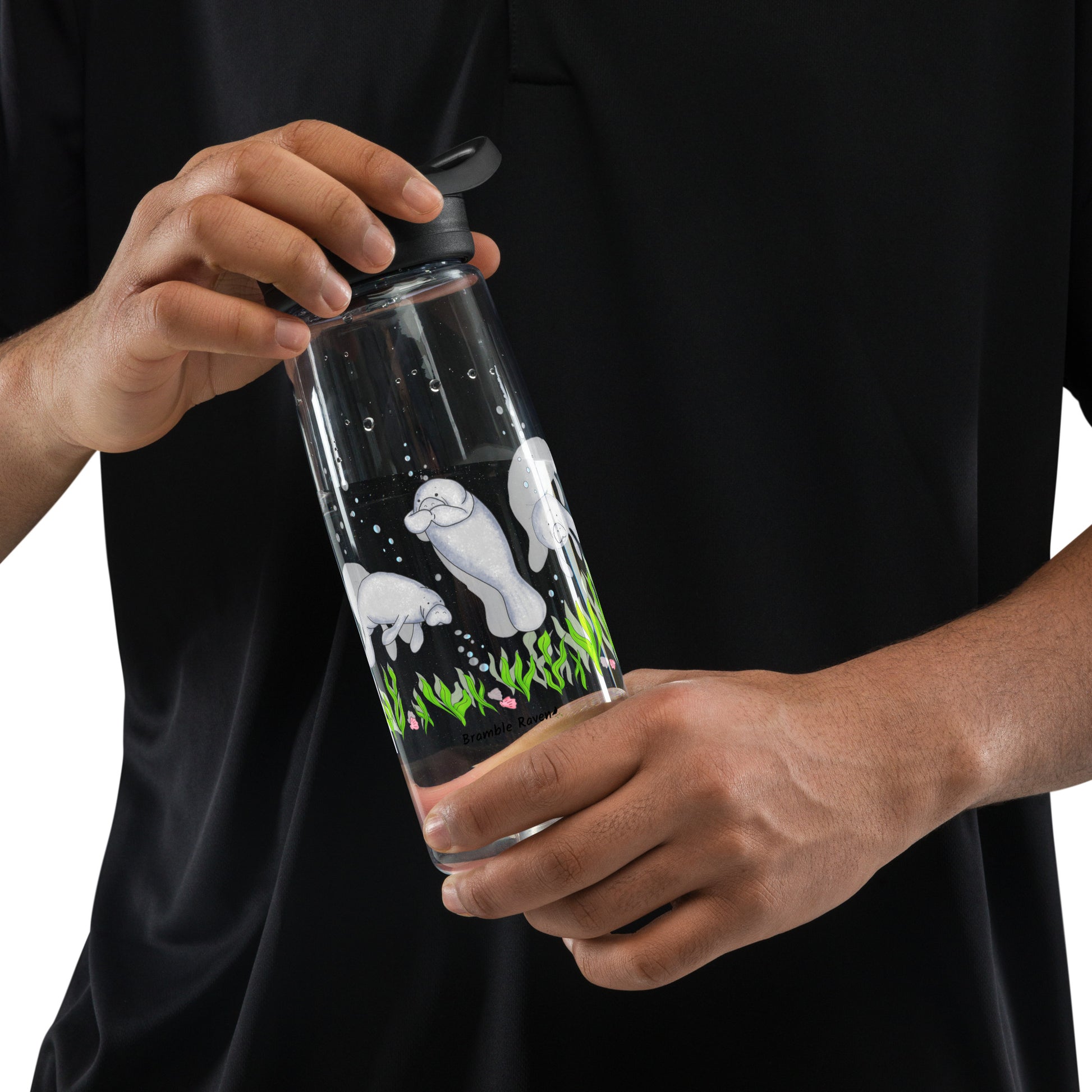 25 ounce sports water bottle with spill proof lid and bite valve. Clear stain and odor-resistant BPA-free plastic with manatee designs around the bottle, swimming above the seaweed and shells. Shown in model's hands.