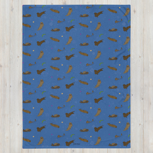 60x80 inch soft polyester blanket. Features pattern of hand illustrated sea otters with accents of sea urchins, seaweed, and shells on an ocean blue background. Blanket has white underside. Machine washable, hypoallergenic, and flame retardant.